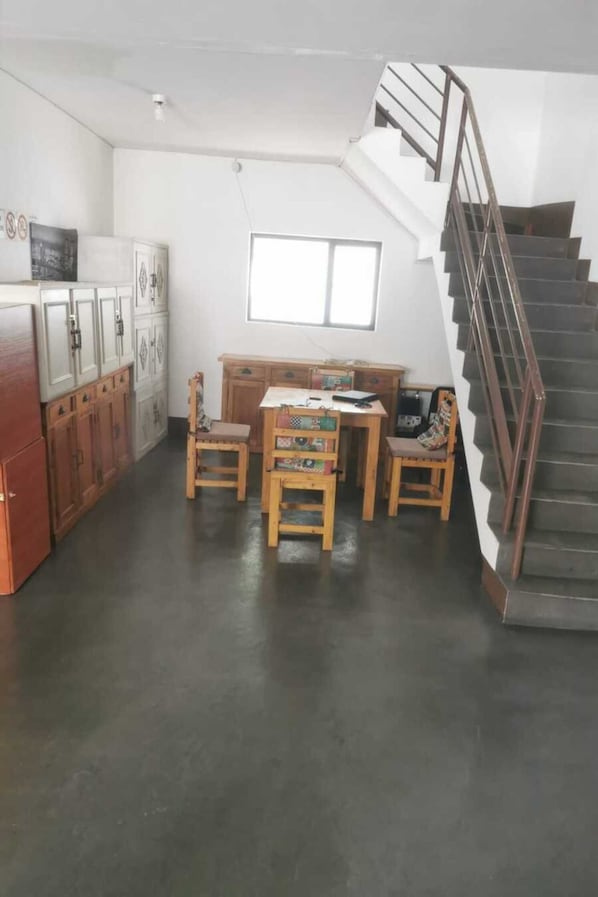 Cozinha espaçosa com armários de madeira, uma mesa de jantar e cadeiras. Uma escada com corrimão de metal é visível à direita.