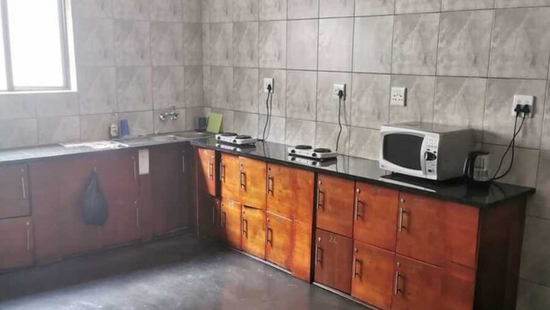 A kitchen with a tiled backsplash, wooden cabinets, a microwave, and a window providing natural light. - White House Guesthouse 29Kew (Johannesburg)
