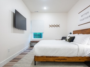 Un dormitorio con cama de madera, televisión montada, ventana con persianas y una obra de arte en la pared con la inscripción 'BETTER TOGETHER'.