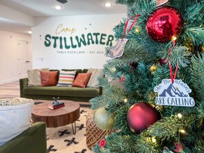 Un salón con un árbol de Navidad, un sofá verde y un letrero que dice "Camp Stillwater".