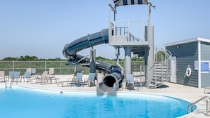 Een zwembad met een glijbaan, ligbedden en een toren voor de badhoeder.