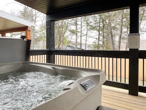 Un jacuzzi en una terraza de madera con vistas a árboles.