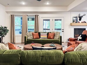 Un salon avec un canapé vert, une table basse ronde en bois et une cheminée décorée d’une tête de cerf.