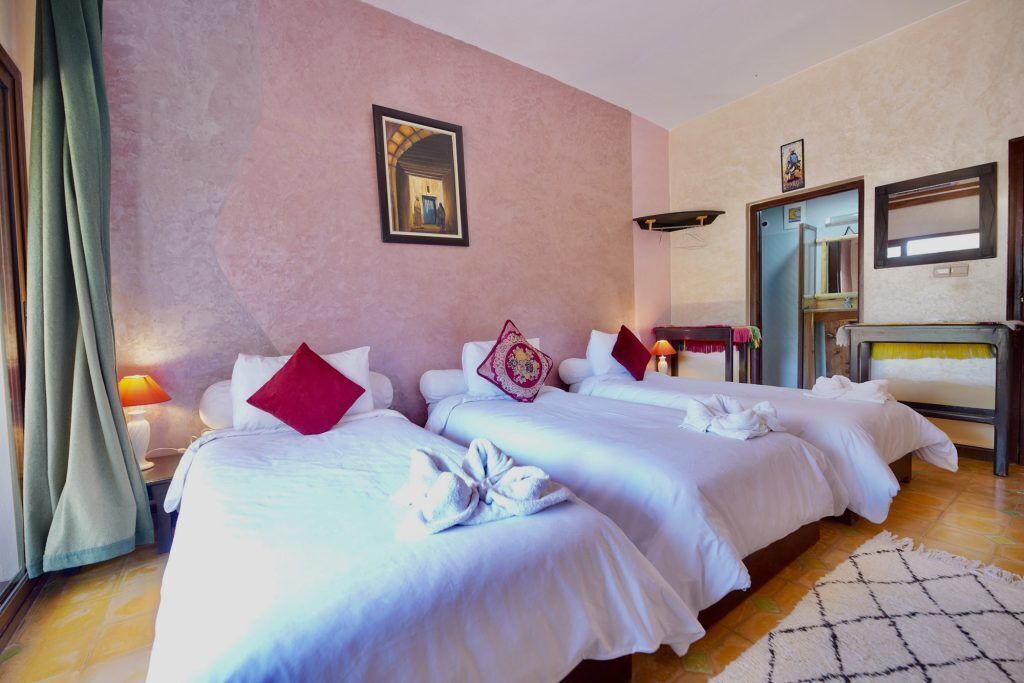 A hotel room with two beds, a mirror, a wardrobe, and a small table with a lamp.