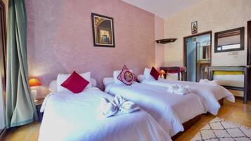A hotel room with two beds, a mirror, a wardrobe, and a small table with a lamp.