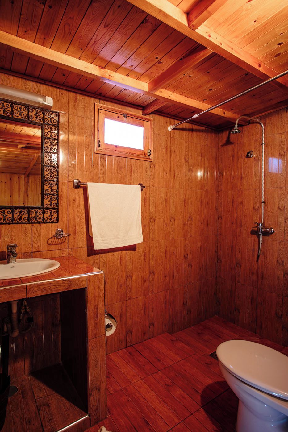A wooden bathroom with a sink, mirror, and toilet.