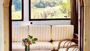 A cozy interior with a wooden bench and a table, a window with a view of a green landscape, and a wooden arch structure. - Dar l'eau vive (Bine el Ouidane)