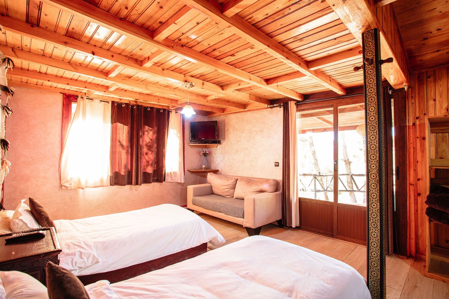 Habitació acollidora amb dos llits, un sofà, una televisió i una finestra amb cortines.