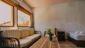 A room with a sofa, a wooden table with a vase, a chair, and a bed. - Dar l'eau vive (Bine el Ouidane)