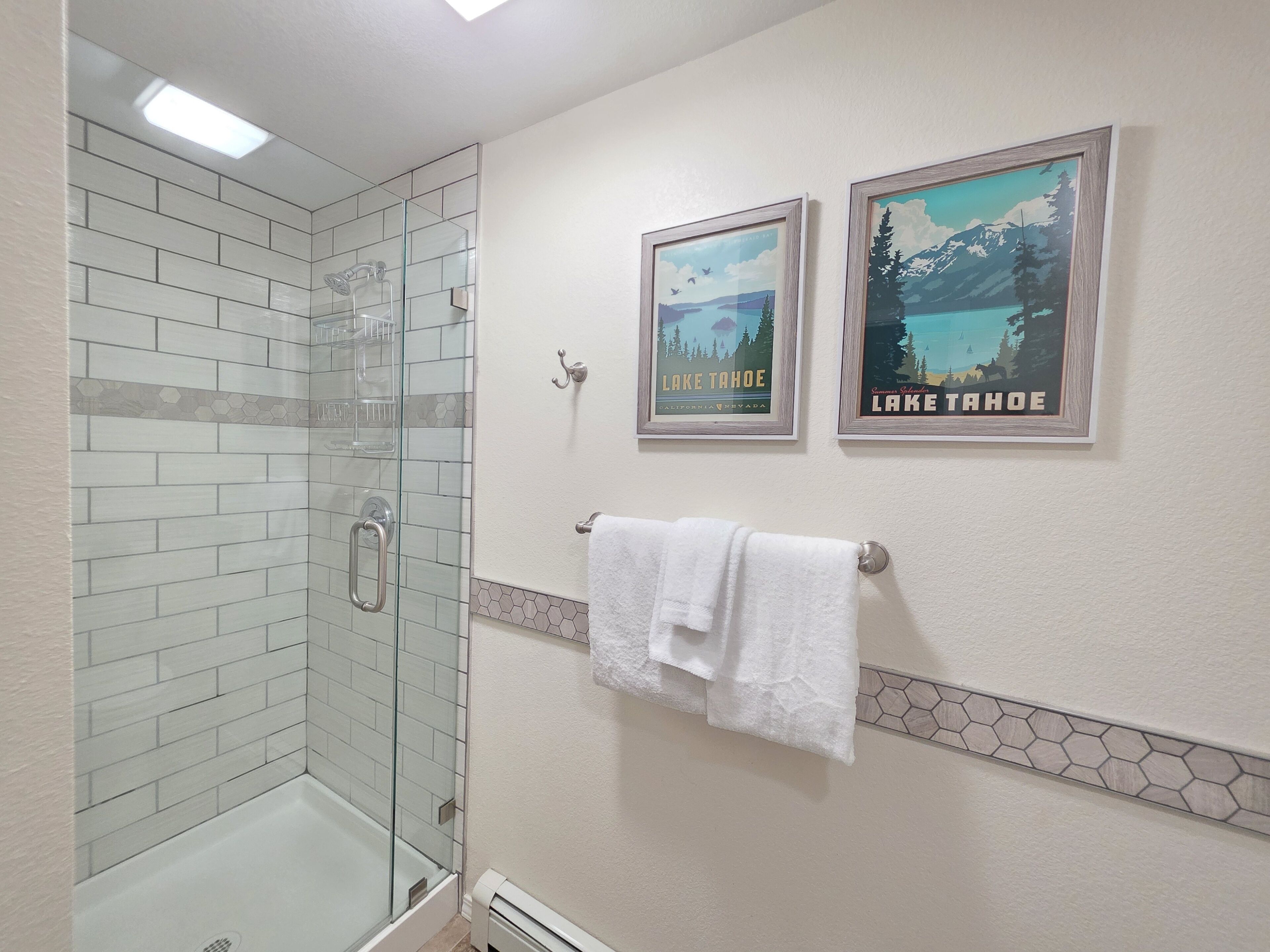 Une salle de bain avec une douche à parois de verre, une serviette blanche suspendue à un porte-serviettes et deux affiches encadrées représentant le lac Tahoe, accrochées au mur.