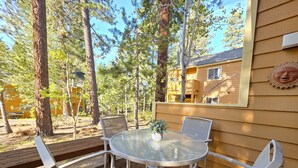 Une terrasse dotée d’une table en verre et de chaises blanches, entourée d’arbres et bordée d’un bâtiment à la façade jaune.