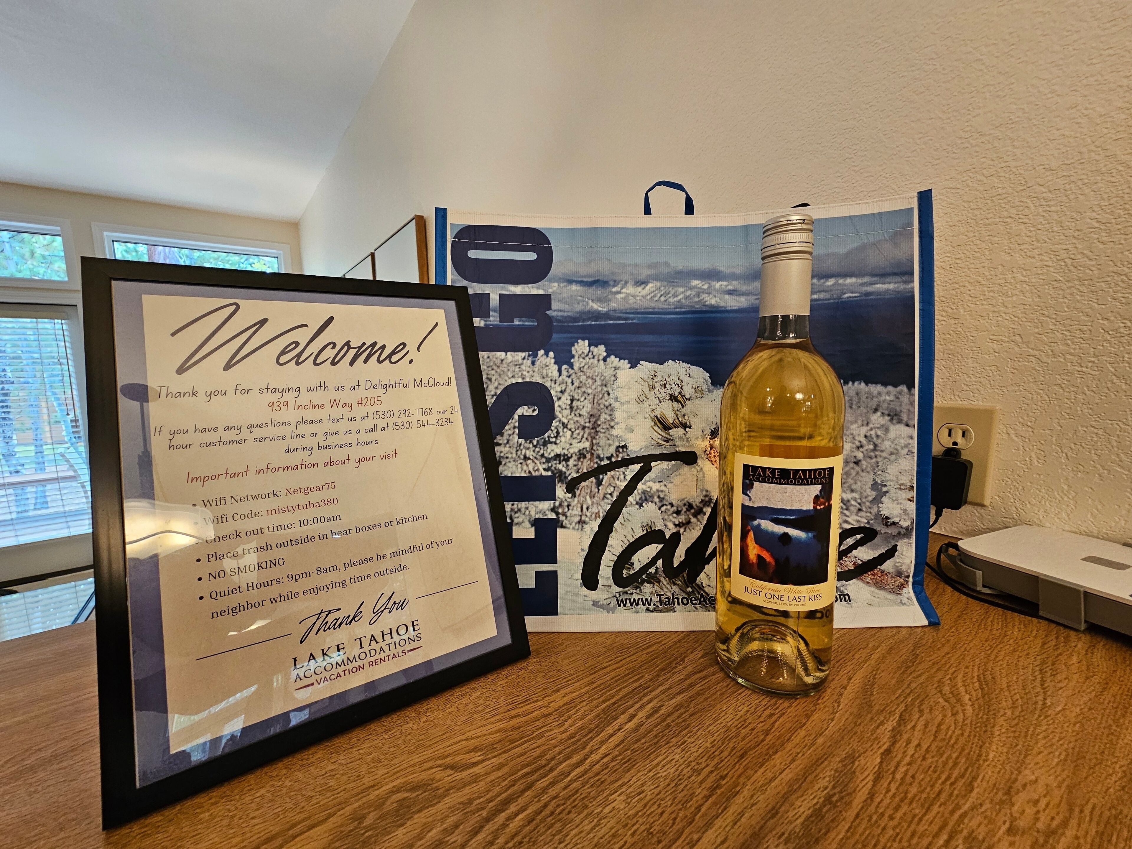Un cartel de bienvenida enmarco con detalles del alojamiento, una botella de vino de Lago Tahoe y un paisaje pintoresco.
