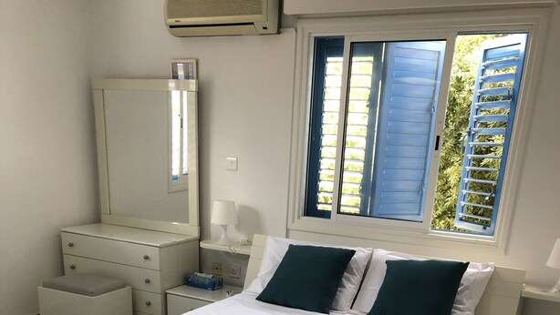 A neatly arranged bedroom with a bed, bedside tables, a dresser, and a window with shutters. - Freshly Refurbished Apartment in Paralimni, Cyprus (Paralimni)