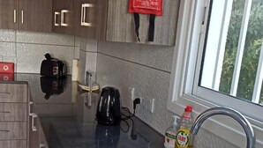 A modern kitchen with wooden cabinets, a black kettle, a red fire blanket, and a dish rack. - Freshly Refurbished Apartment in Paralimni, Cyprus (Paralimni)