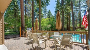 Un espace extérieur abrité comprenant une piscine, une terrasse en bois et de grands arbres.