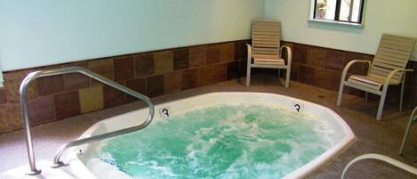 A hot tub with a metal ladder, surrounded by chairs, in a room with tiled walls and a window.