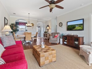 A spacious living room with a red sofa, a wooden coffee table, a television, and a ceiling fan.