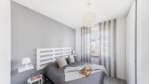 Un dormitorio moderno con una cama grande, una mesita de noche con lámpara y vistas al exterior a través de una ventana con cortinas.
