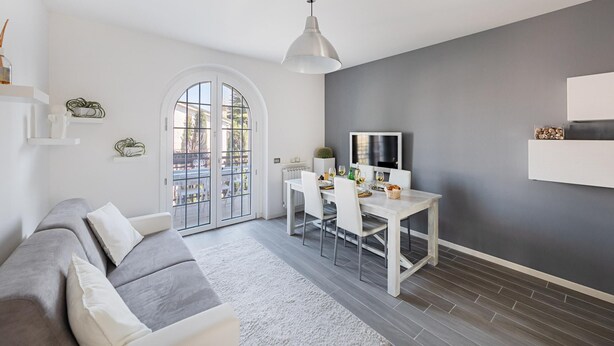 Una sala de estar moderna con un sofá gris, una mesa de comedor para dos personas y una pared de acento gris.