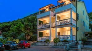 A multi-story building with balconies, a stone staircase, and a parking area with cars. - Apartments Gulin (Sibenik)
