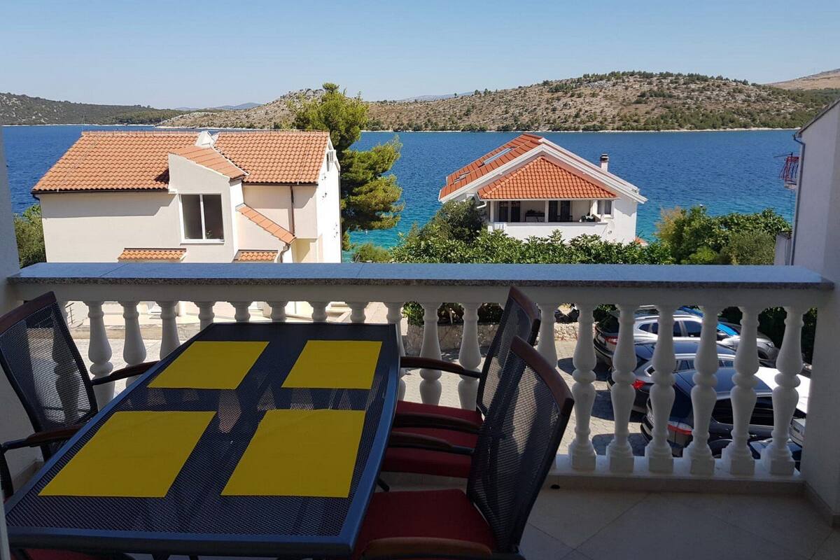 A balcony with a table and chairs, overlooking a body of water and buildings.