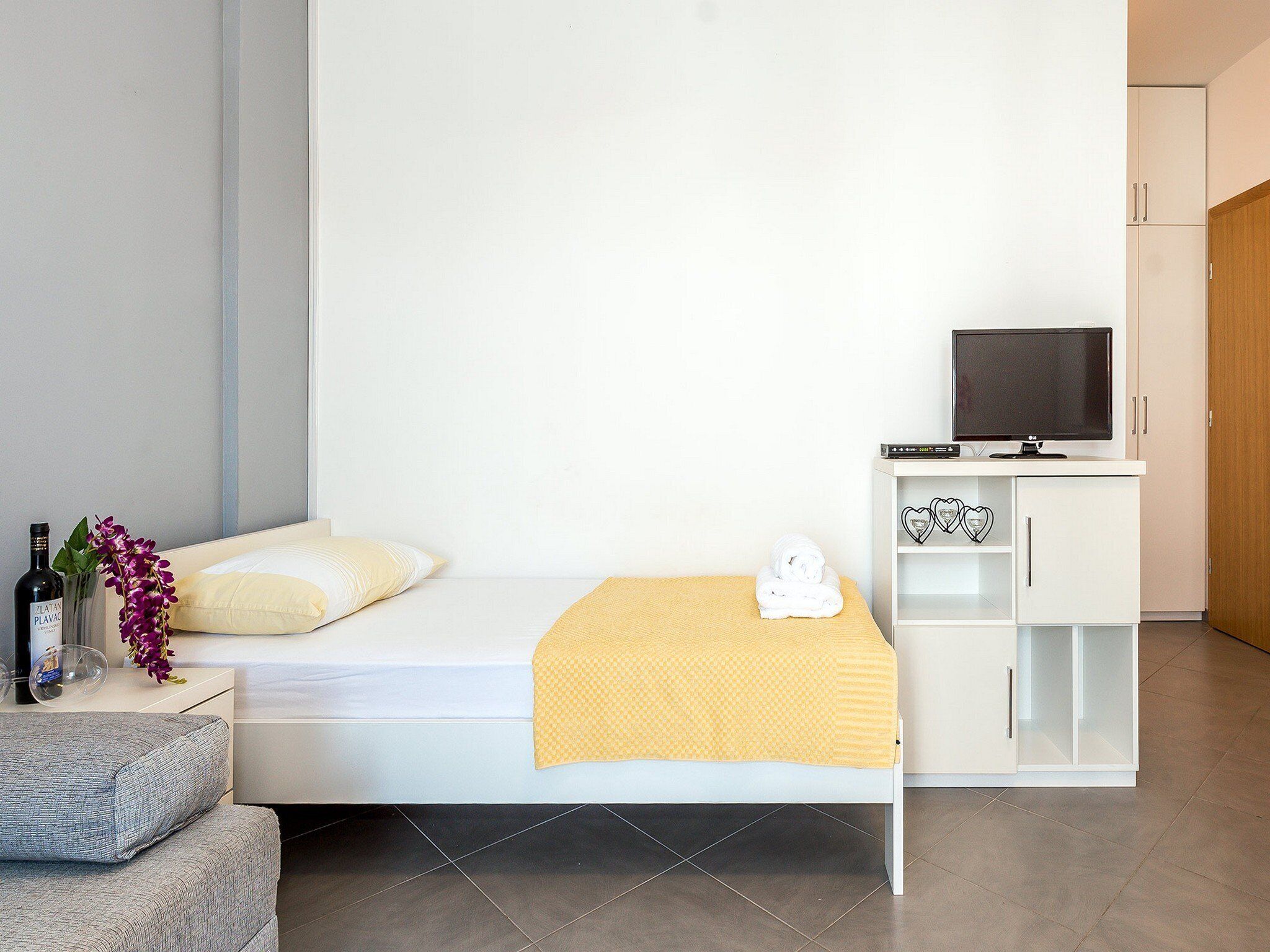 A minimalist bedroom with a bed, a TV, and a small white cabinet.