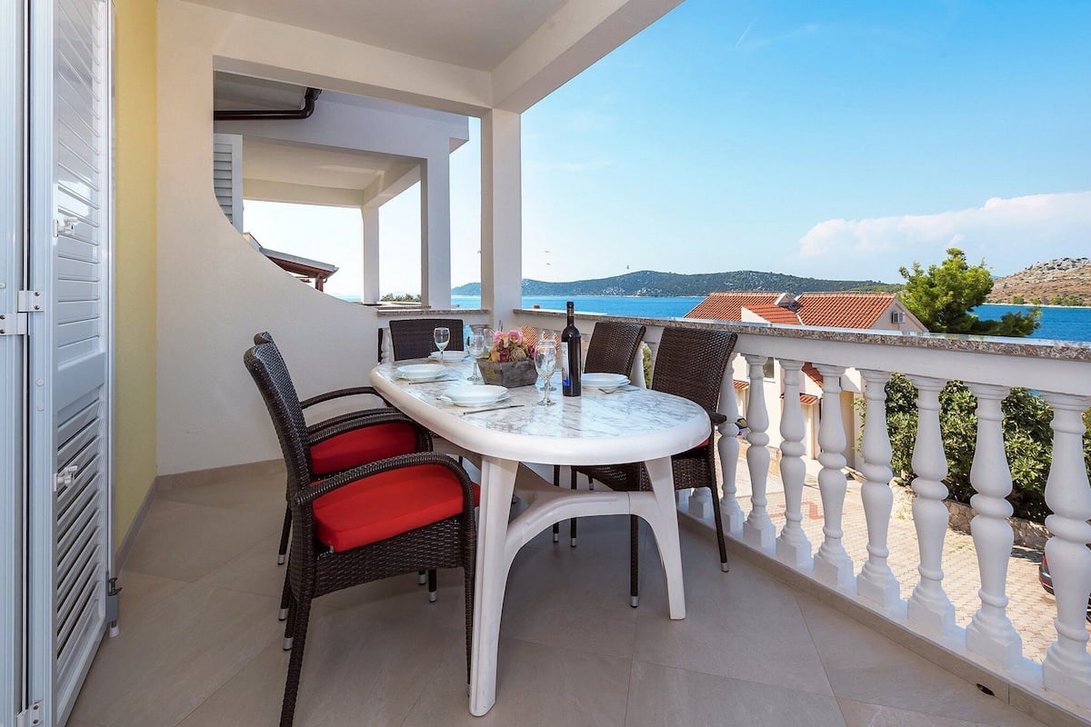 A balcony with a table set for two, overlooking a scenic view of the sea and hills.