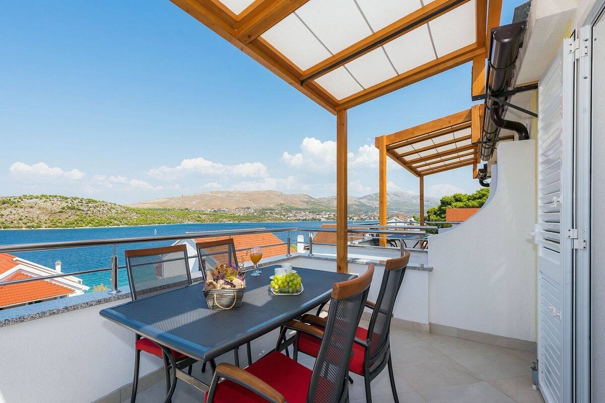 A balcony with a table, chairs, and a view of the sea.