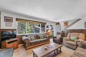 A living room with a large window, a television, a sofa, a chair, and a coffee table. - Foothill Folly 4 Bedroom Home by RedAwning (Zephyr Cove)