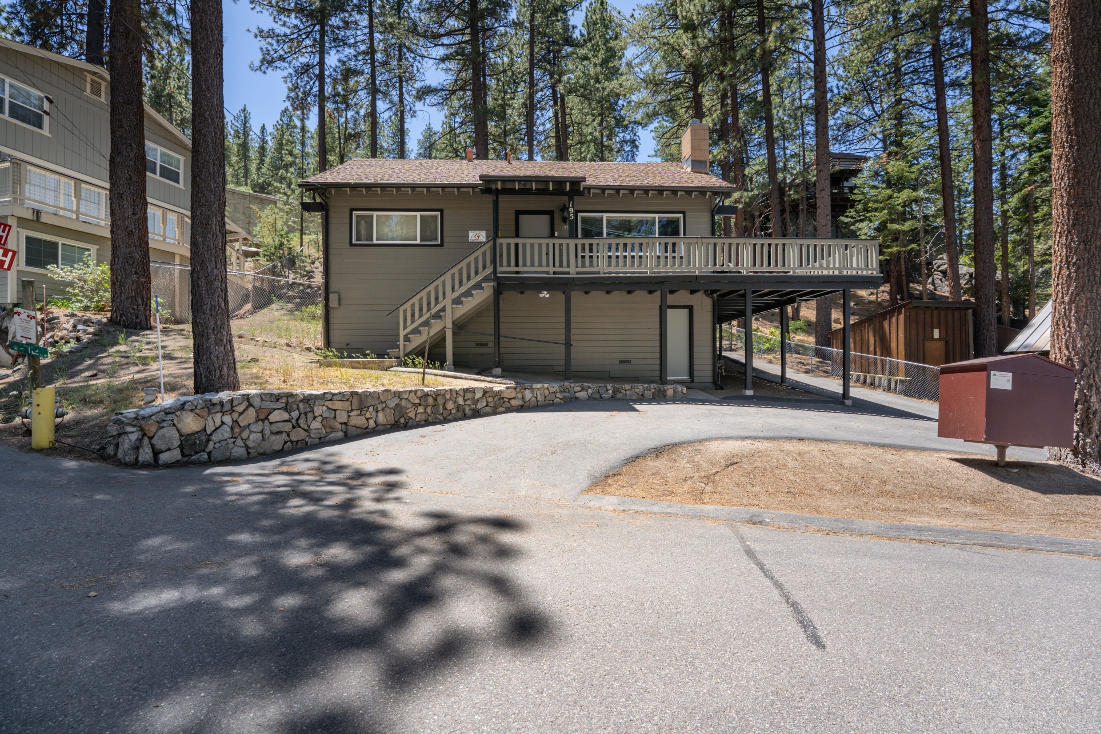 A two-story building with a balcony, a stone retaining wall, and a paved driveway.