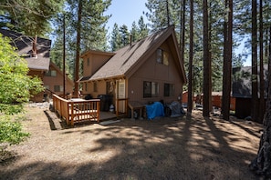 A cabin with a deck, surrounded by tall pine trees. - Cozy Mountain Hideaway 3 Bedroom Home by RedAwning (Incline Village)