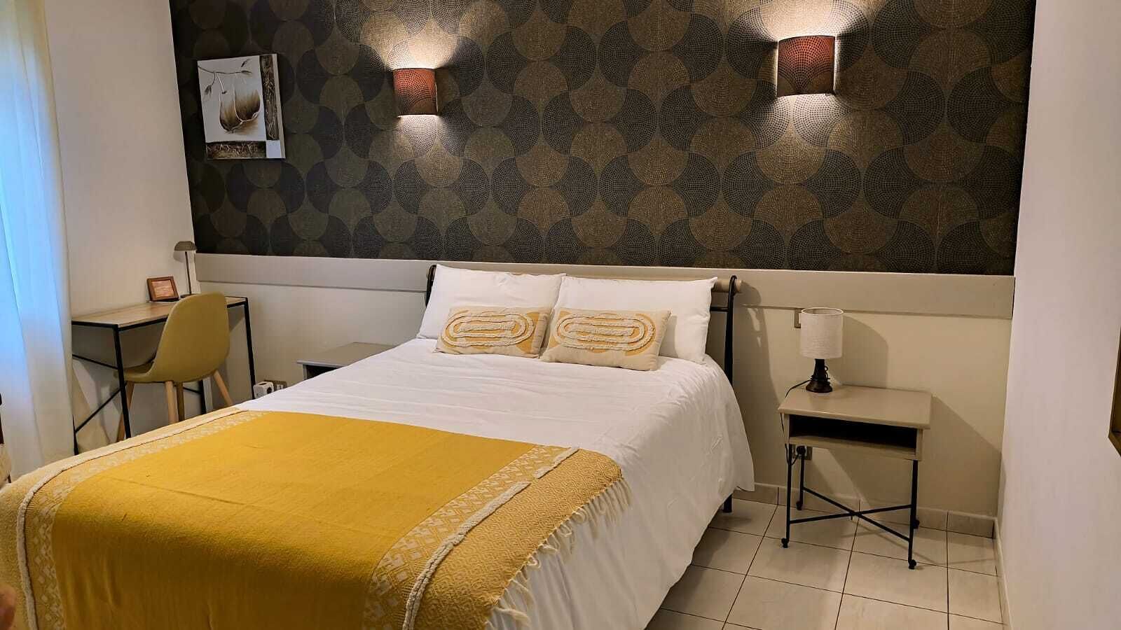 A neatly made bed with a yellow throw blanket, a bedside table with a lamp, and a chair.