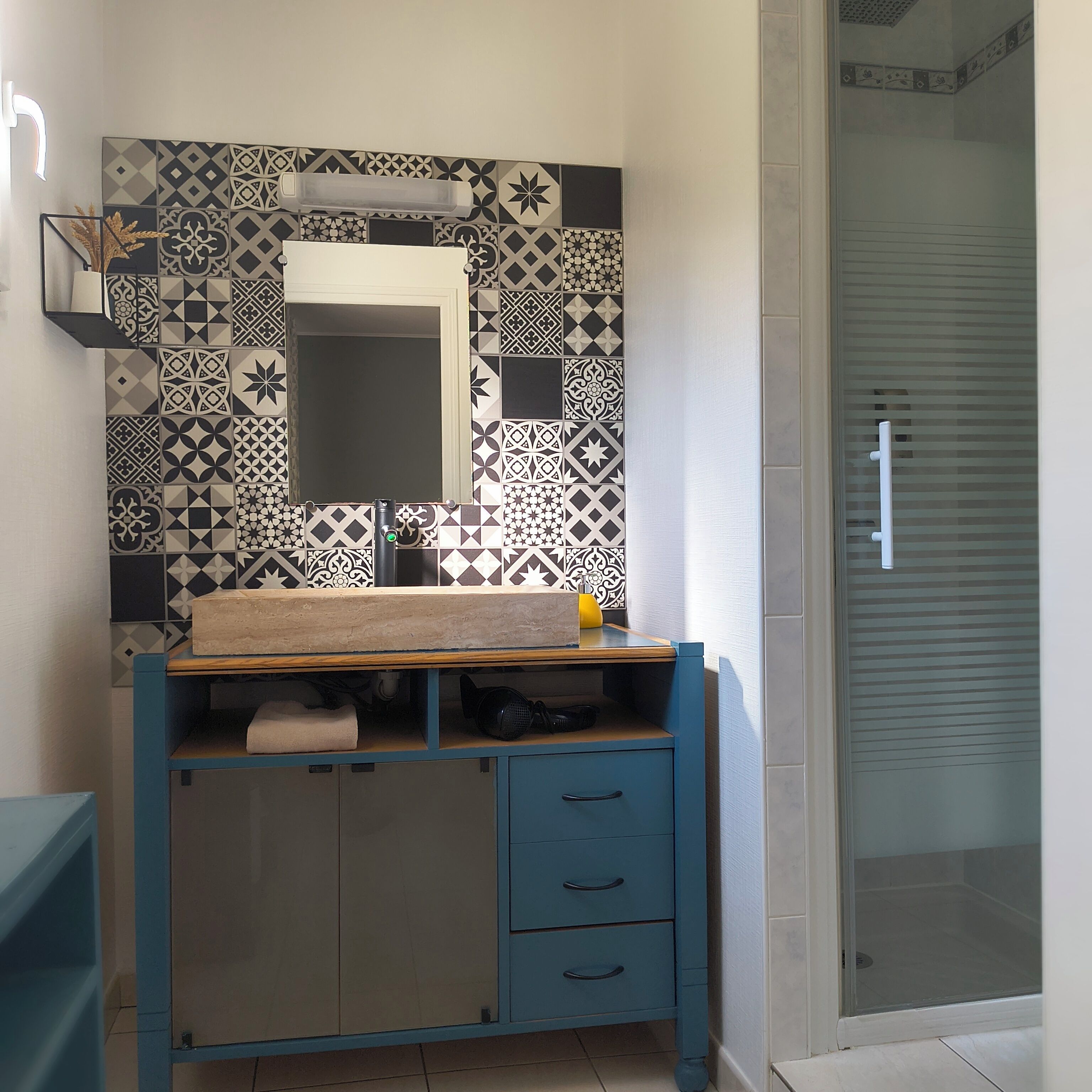 Une salle de bain avec un mur recouvert de carreaux, un miroir, un lavabo avec un plan de travail en bois et un meuble bleu avec des tiroirs.