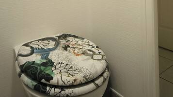 Une salle de bain comprenant des toilettes, un interrupteur fixé au mur et une étagère décorative agrémentée d’une plante et d’un diffuseur de parfum à bâtonnets.