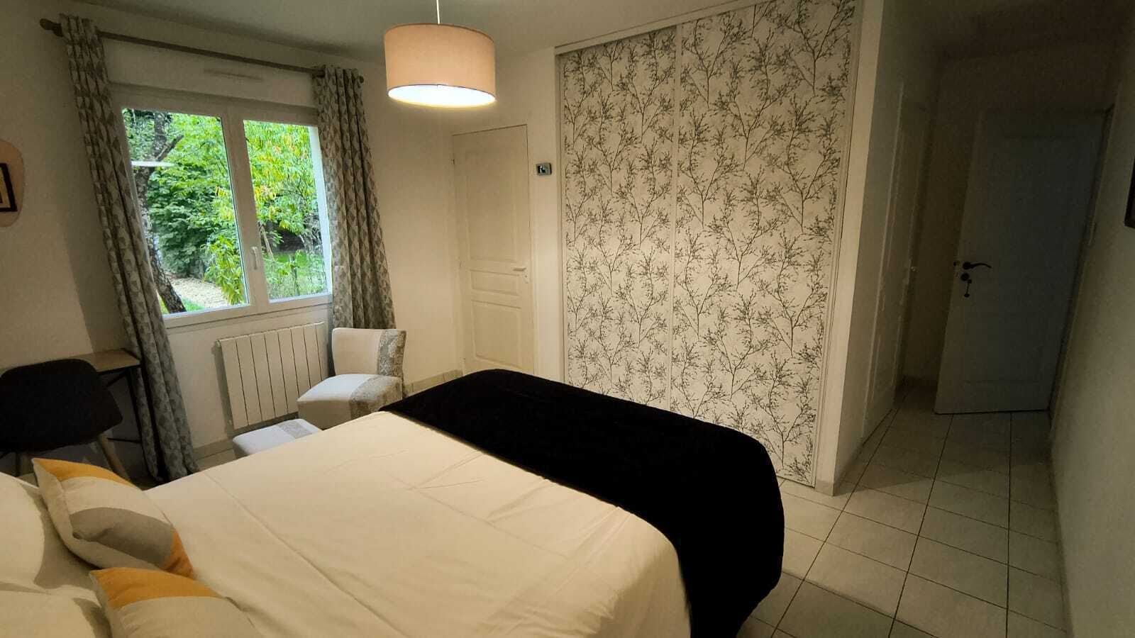 A bedroom with a bed, a chair, a radiator, a window with curtains, and a door.