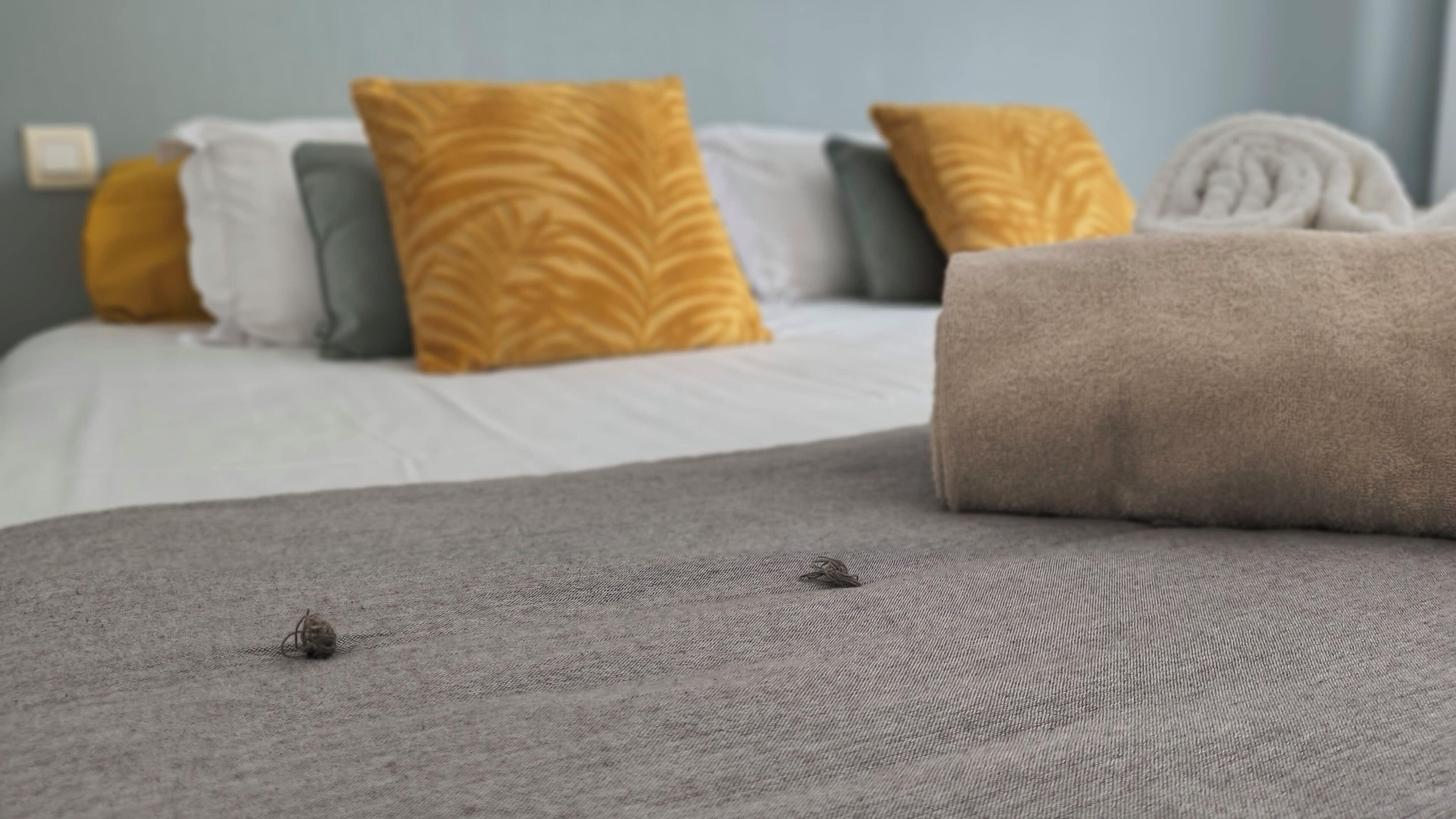 A neatly made bed with a grey bedspread and two pillows, one yellow and one white.