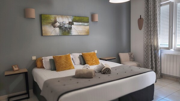 Habitación de hotel con cama, mesita de noche, una silla, un cuadro en la pared y ventana con cortinas.