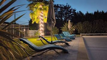 Zona de piscina exterior con sillas de descanso y palmeras.