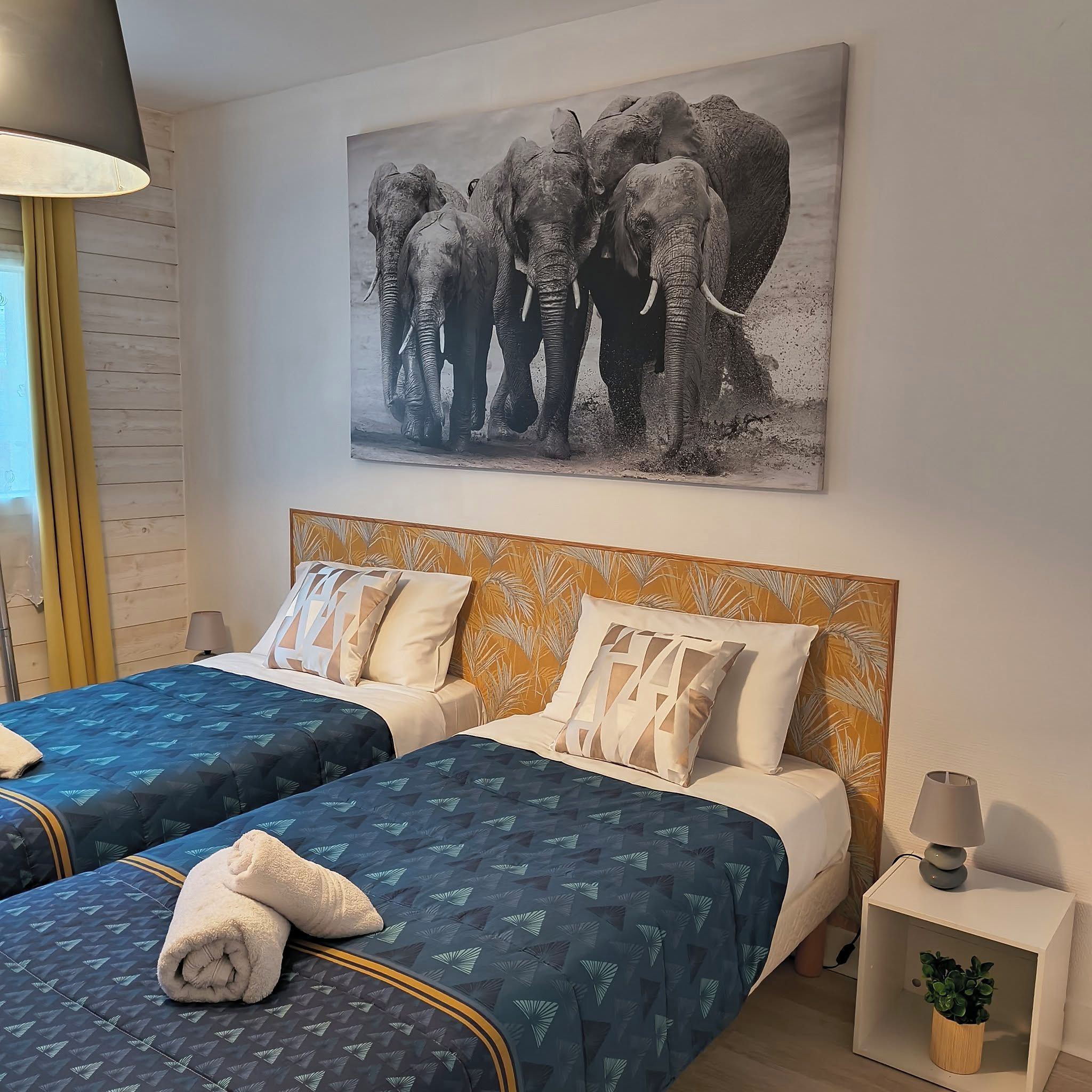 A hotel room with two beds, a large elephant painting on the wall, and a nightstand with a lamp and a plant.