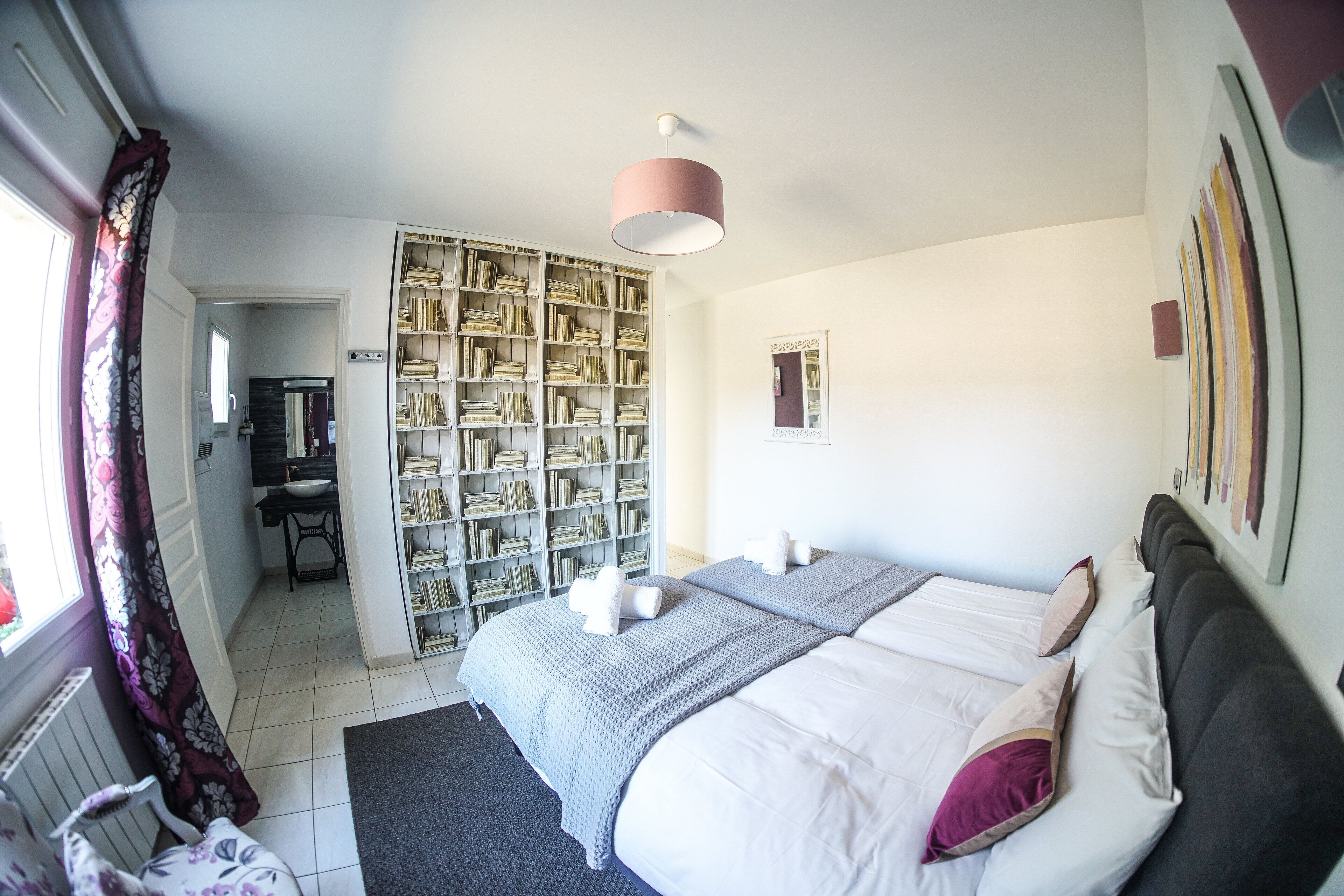 A bedroom with a large bed, a bookshelf, a desk, and a window with curtains.