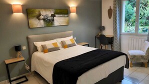 Un dormitorio con cama, mesitas de noche, lámpara, silla y ventana con vistas a vegetación.