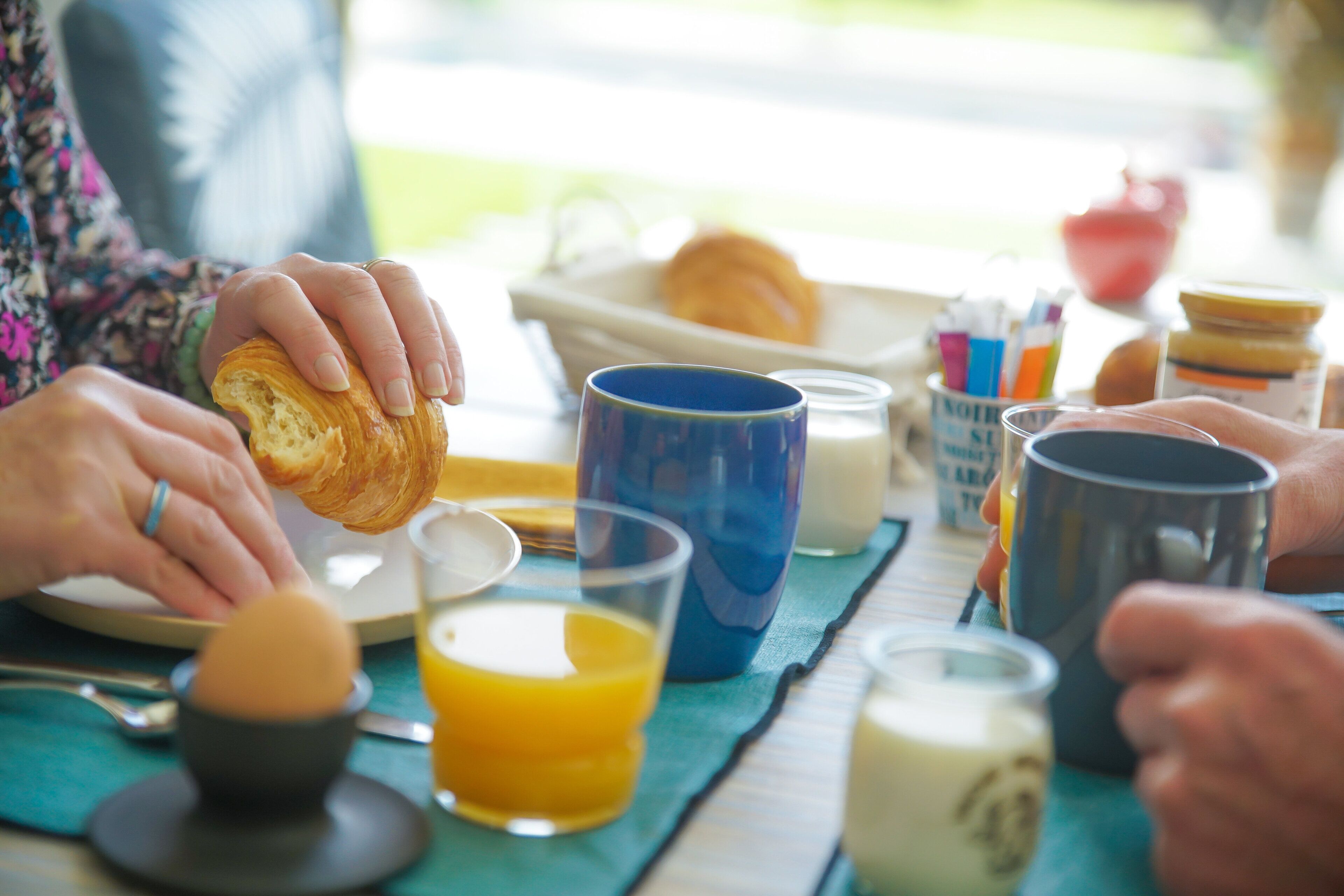 A breakfast setting with a croissant, orange juice, and various mugs on a table.