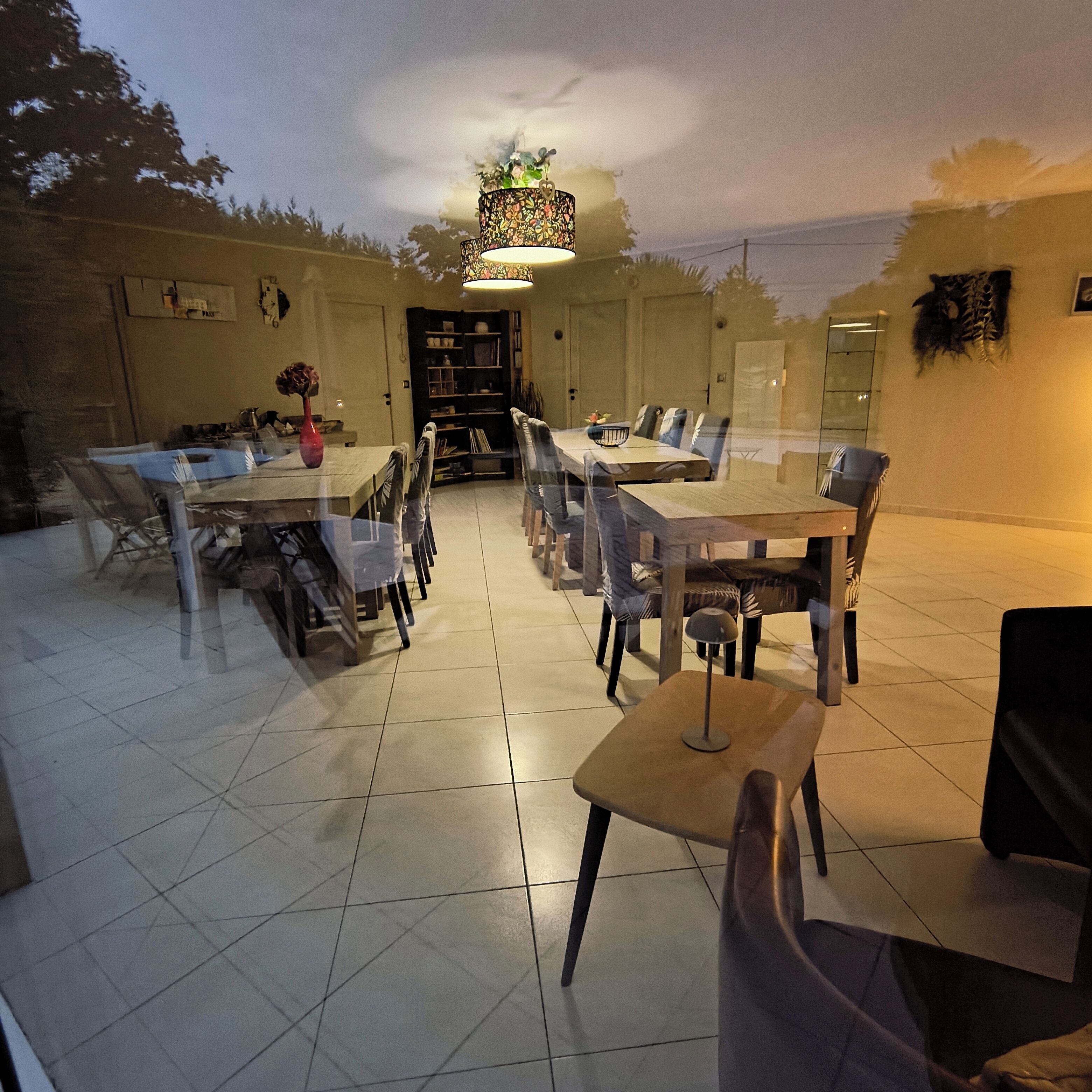 An outdoor dining area with a large table and chairs, a bookshelf, and a decorative ceiling light.