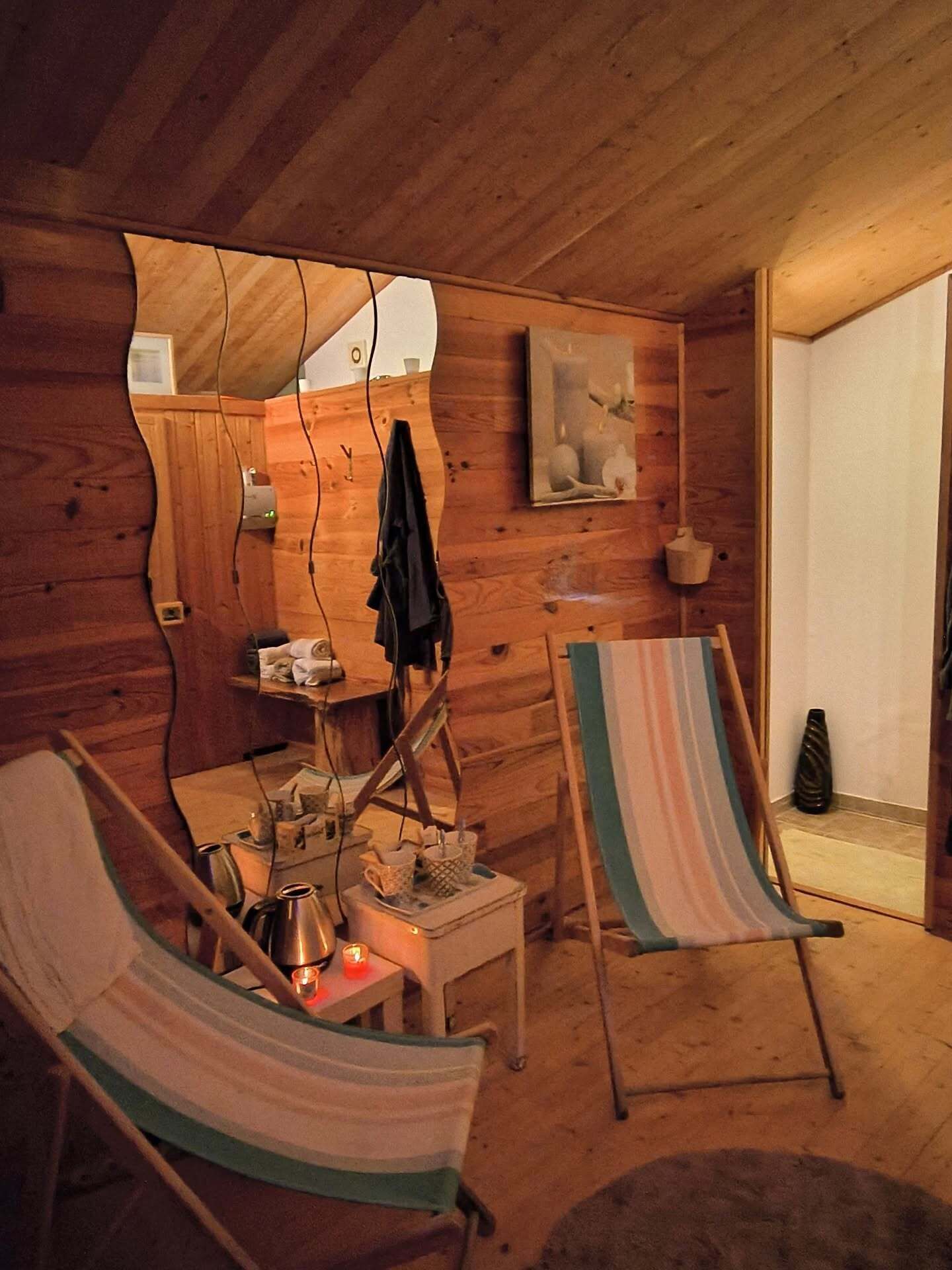 Interior acogedor de una cabaña de madera con dos hamacas, una mesita con una tetera y un espejo que refleja la habitación.