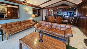 A spacious living room with leather sofas, a coffee table, and a kitchen area visible through an open doorway.