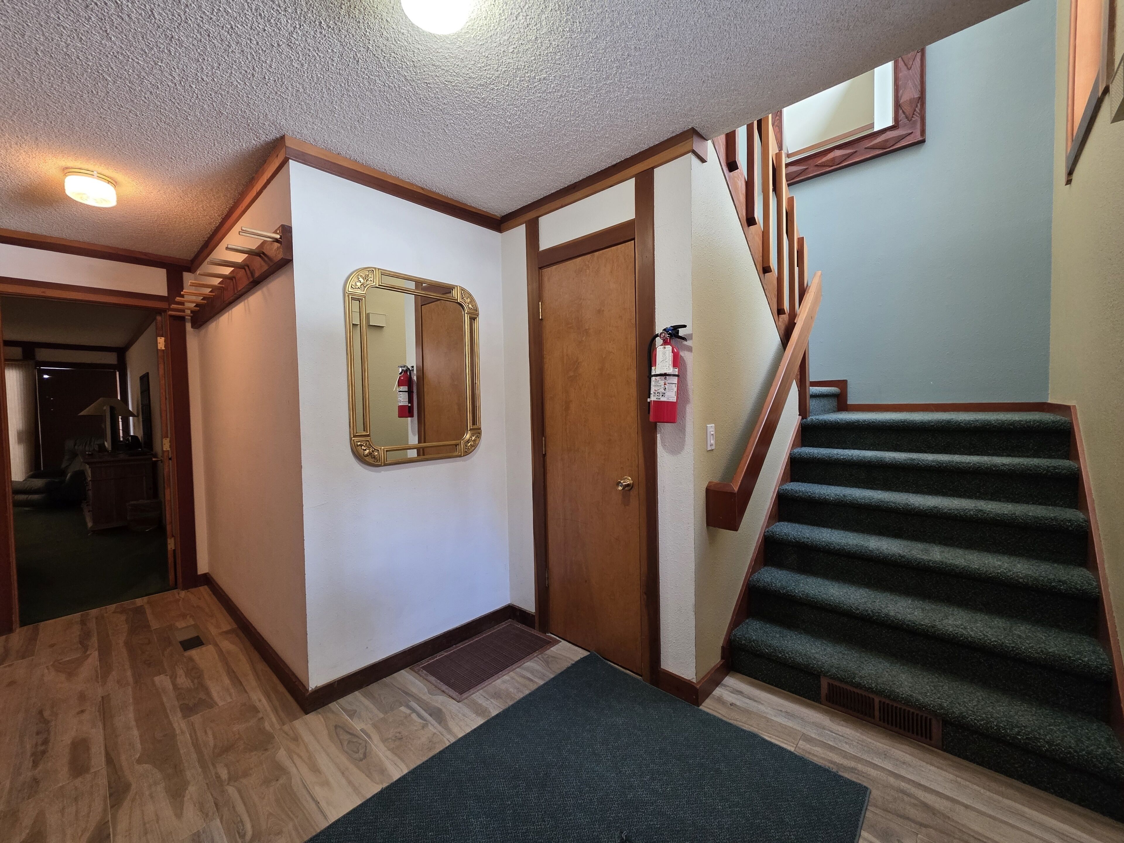 A hallway with a wooden staircase, a fire extinguisher, and a mirror on the wall.