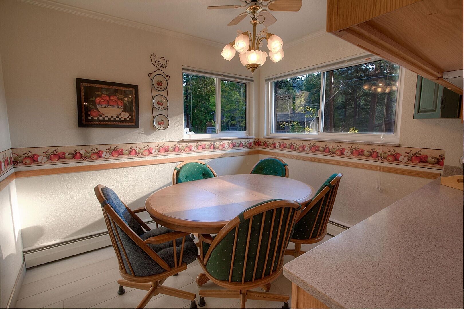 A kitchen with a round table and four chairs, large windows, and a ceiling fan.