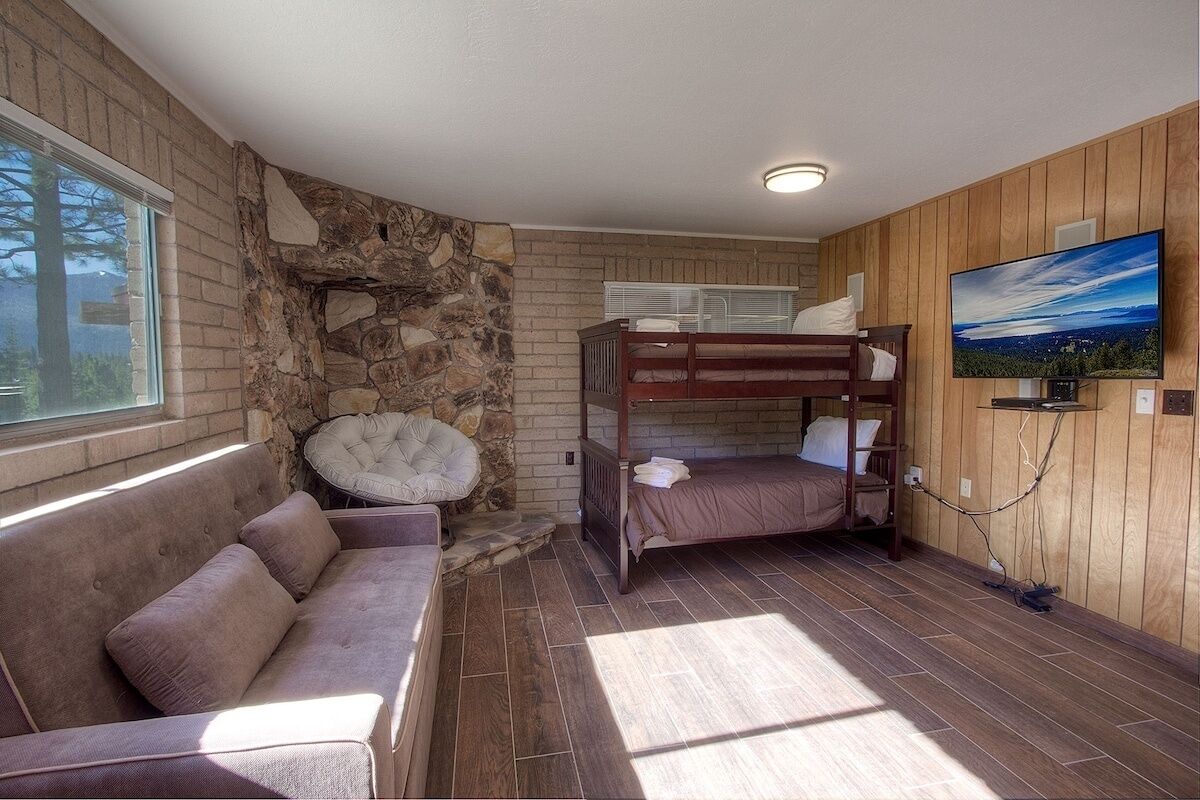 A cozy room with a bunk bed, a cushioned bench, a stone wall, and a television on the wall.