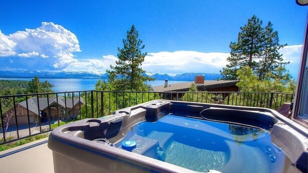 A hot tub on a balcony with a view of a lake and mountains.