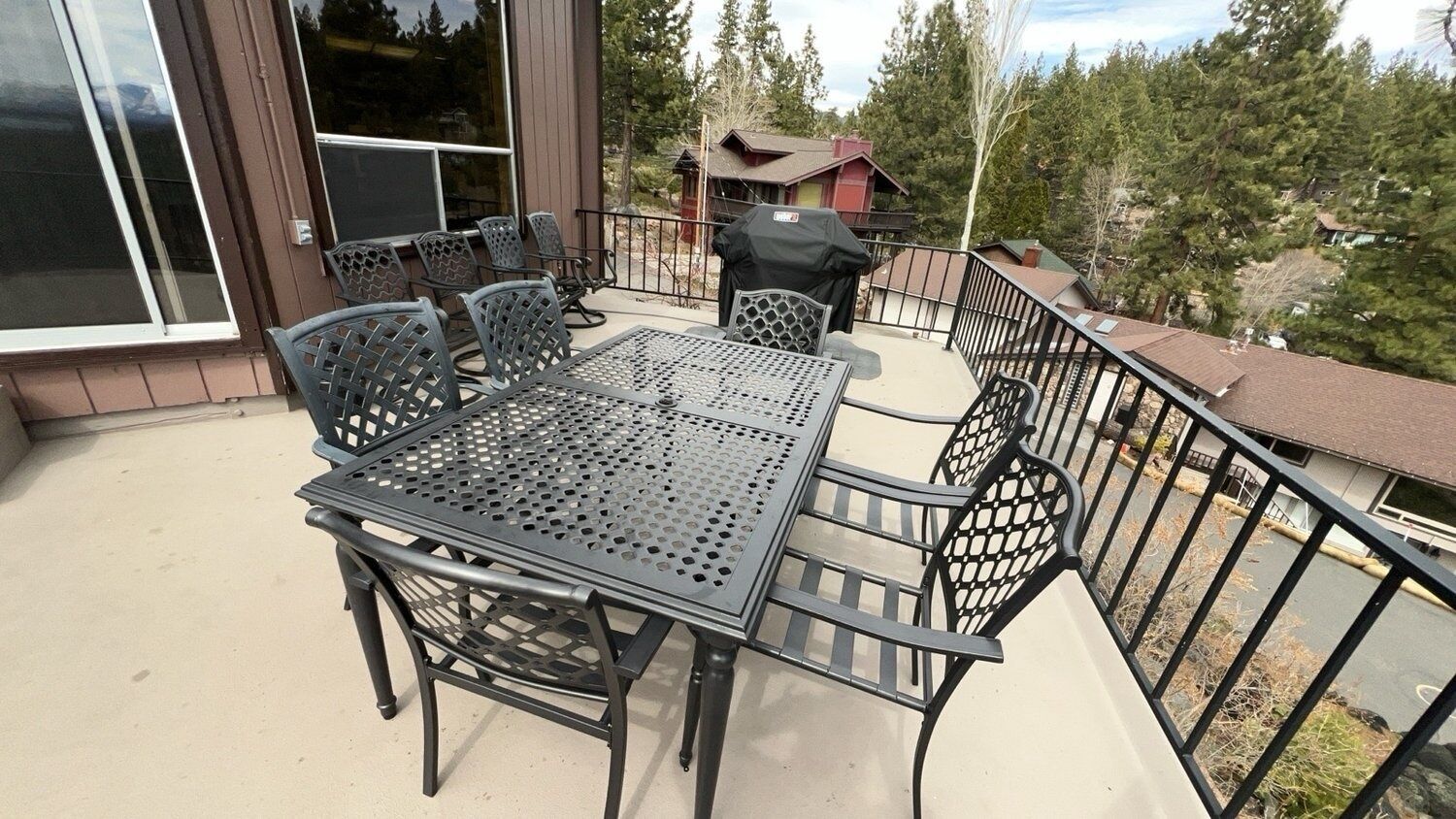 Een terras met een metalen tafel en stoelen, een barbecue en uitzicht op een bebost gebied.